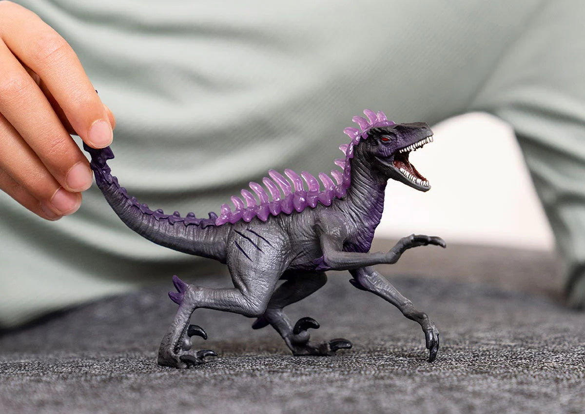 Shadow Raptor toy figure with sharp teeth, claws, and purple spikes, held by a hand on a gray surface.