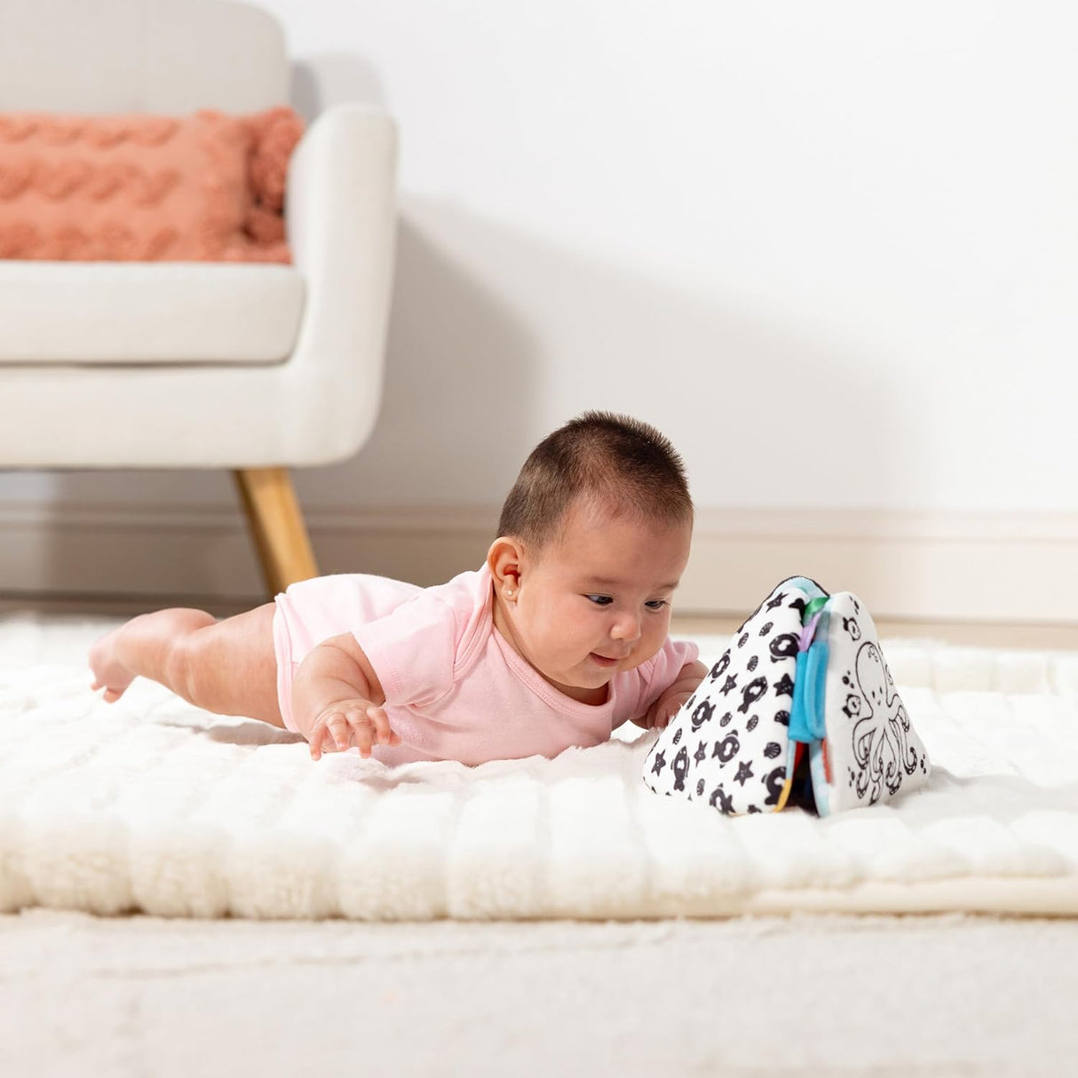 Baby lying on tummy engaging with the black and white Ocean Tummy Time Triangle toy on a soft mat.