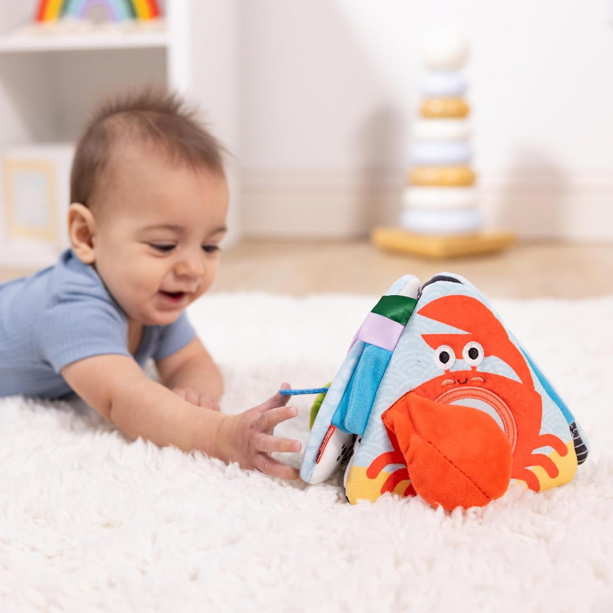 Baby reaching for the colorful Ocean Tummy Time Triangle cloth toy with ocean-themed interactive panels.
