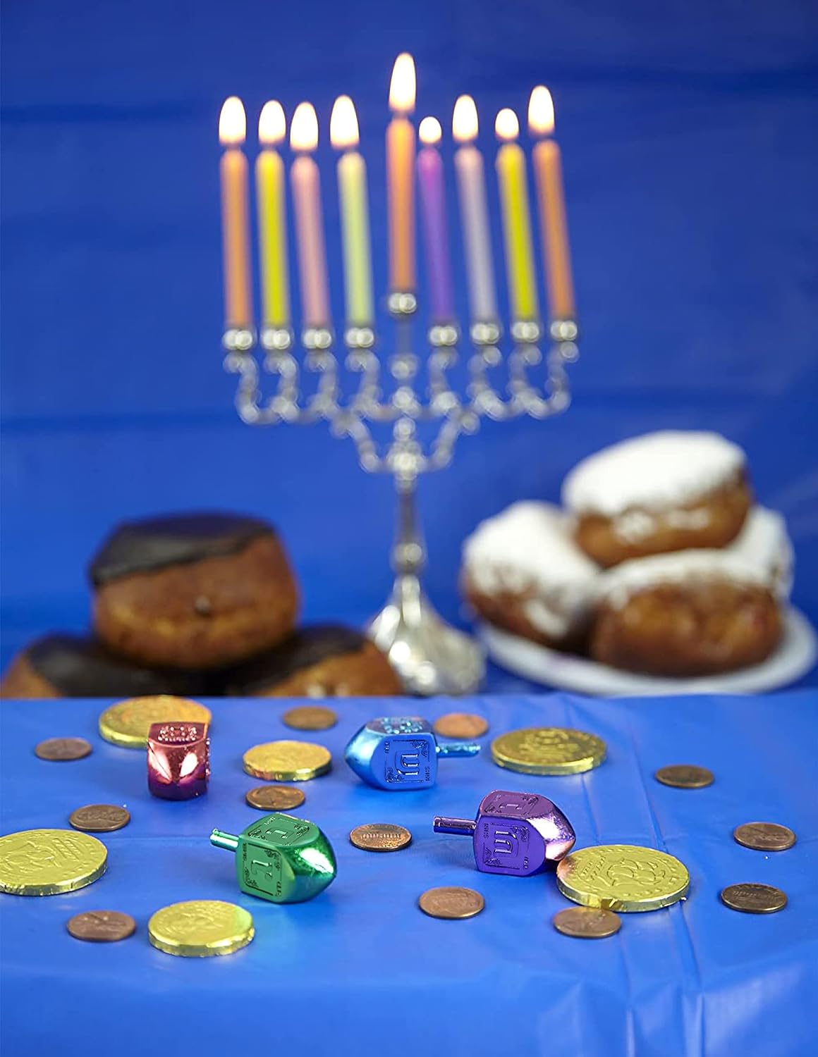 Dreidel | Metallic Plastic colorful spinning tops with gelt and Chanukah menorah in background on blue tablecloth