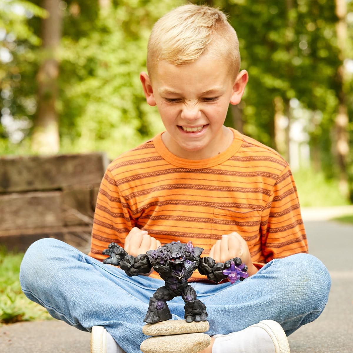 Child playing outdoors with Eldrador Creatures Shadow Stone Monster figure balancing on stones in sunlight.