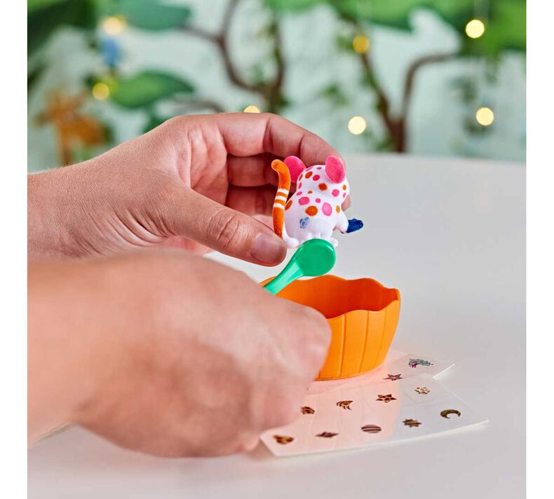 Hands decorating a colorful animal figurine from the Scribble Scrubbie Treehouse set with stickers and accessories.