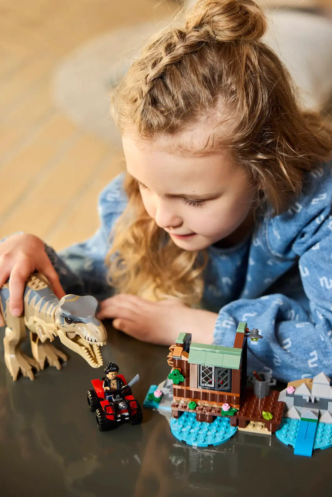 Child playing with LEGO Jurassic T. Rex River Escape set featuring T. rex, minifigures, shed, boat, and ATV.