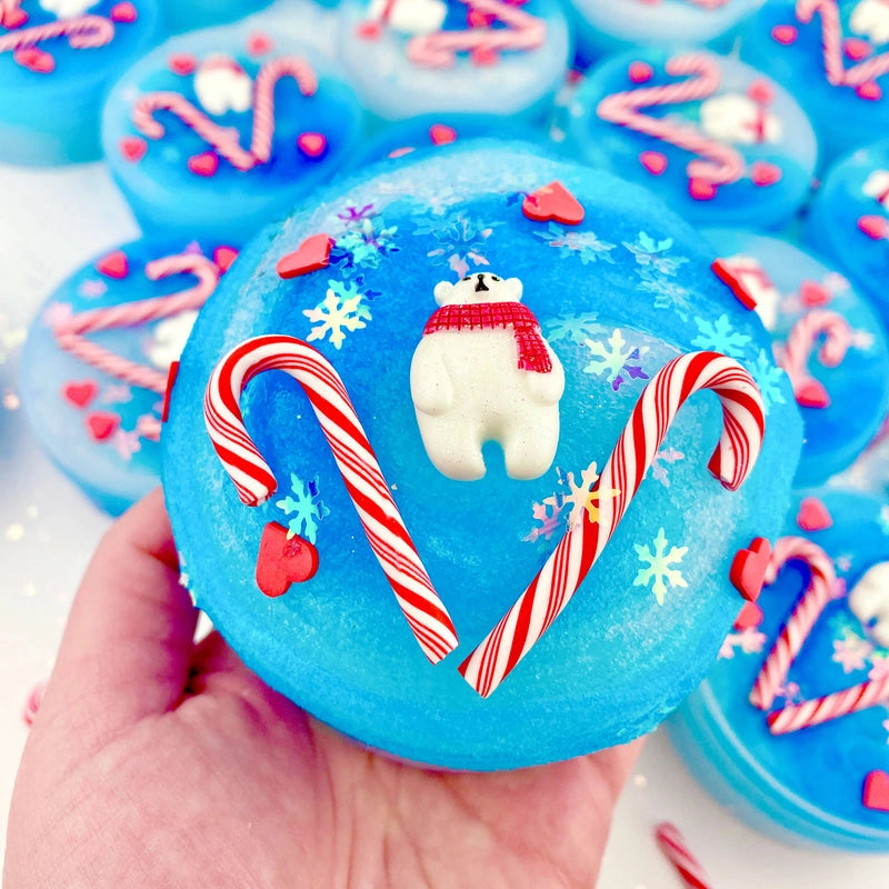 Hand holding Arctic Icee Cola Soda Jelly Slime with polar bear charm, candy canes, and snowflake decorations.
