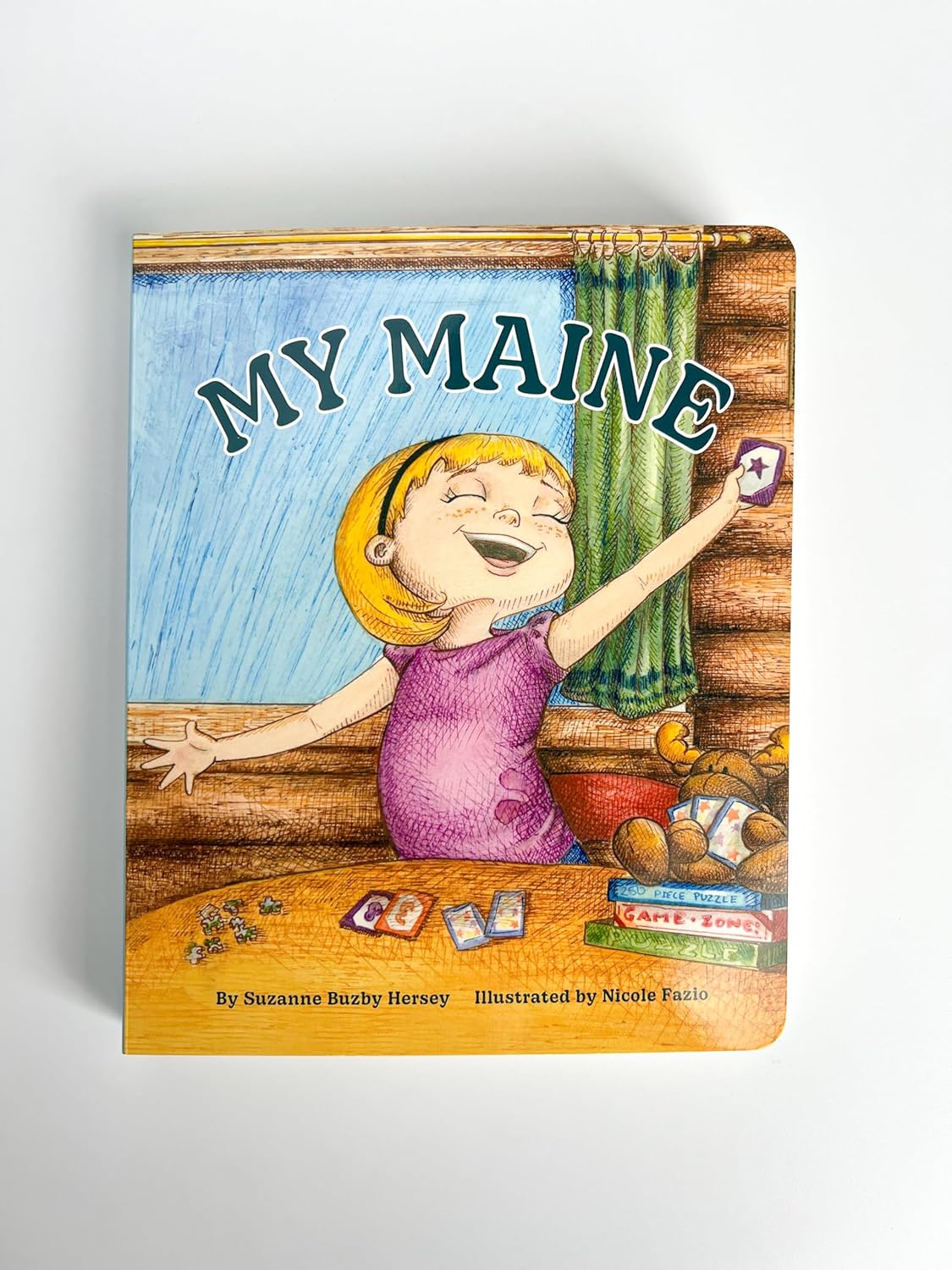 My Maine" children's board book cover featuring a smiling girl playing cards in a cozy cabin setting.