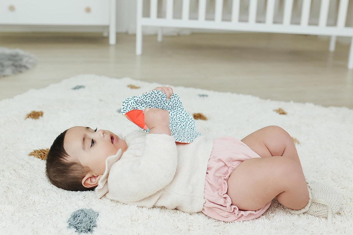 Baby lying on rug holding Feel to Learn Leaf Mirror with crunchy edges and colorful pattern.