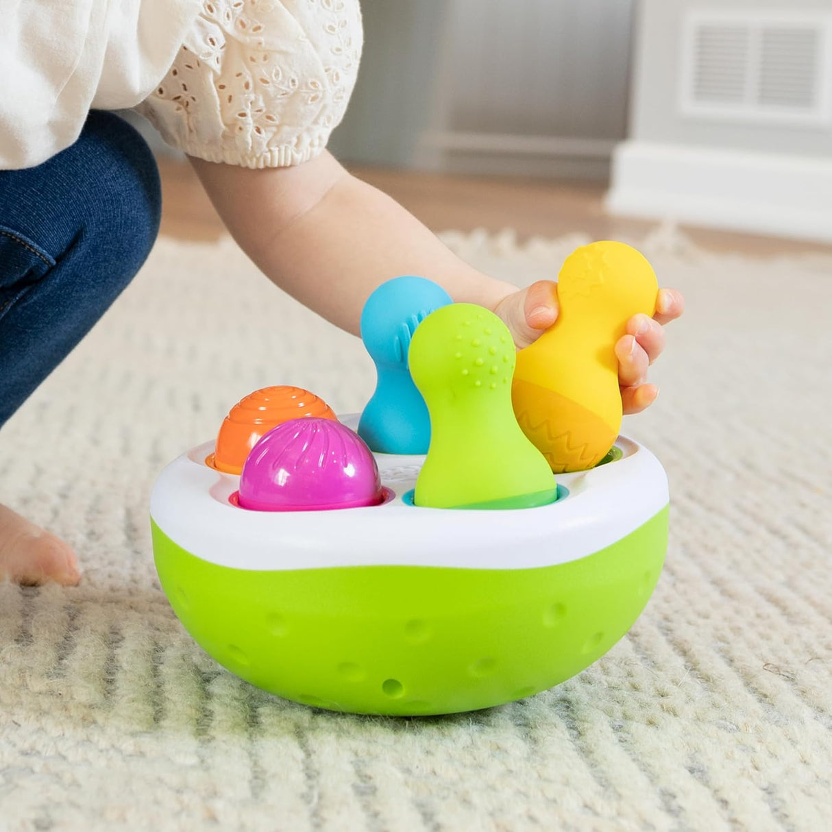 Child playing with colorful textured pins and wobbling bowl in SpinnyPins toy for sensory and motor skill development.
