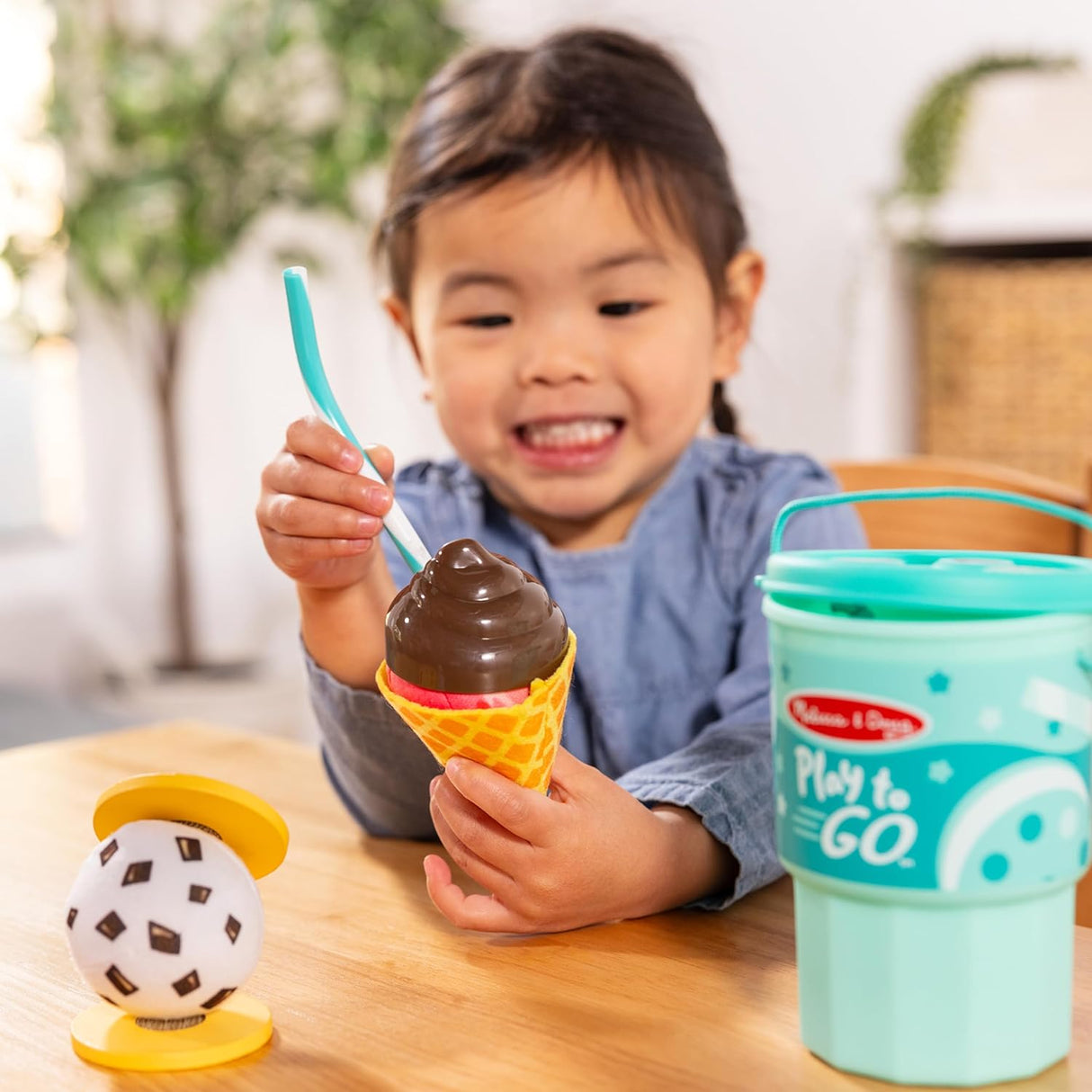 Child playing with chocolate ice cream cone toy from Play to Go Cake & Cookies Play Set in turquoise cup.