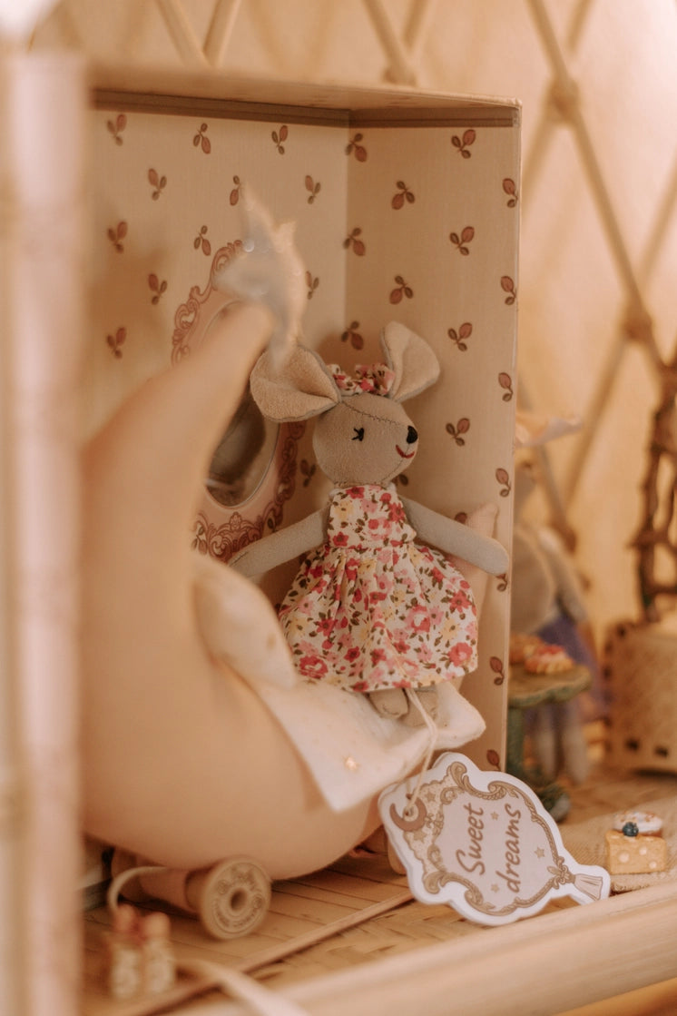 Cozy mouse doll wearing floral dress sitting in a soft moon bed with delicate background patterns and sweet dreams tag