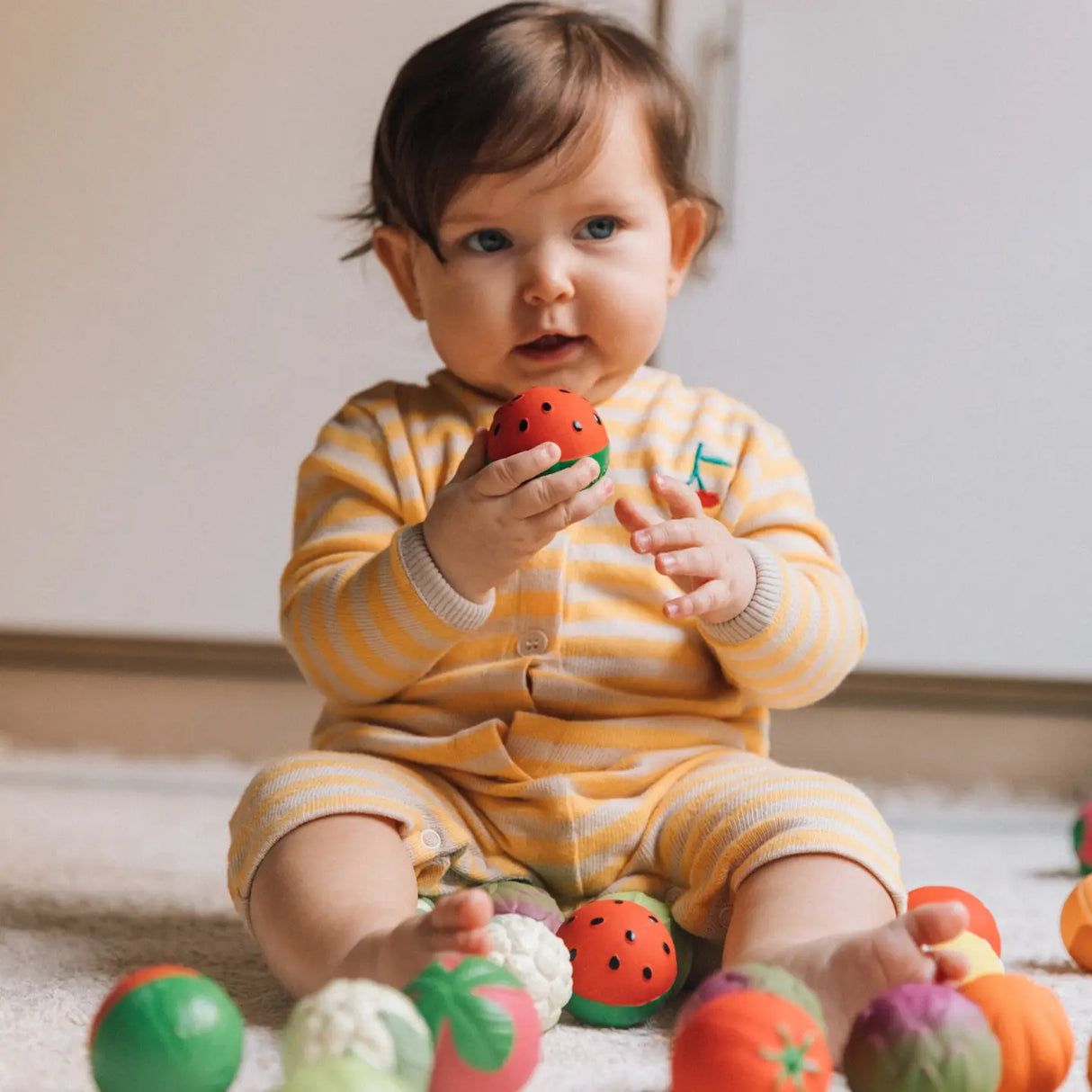 Baby in striped outfit playing with colorful sensory fruit balls for teething and fine motor skill development