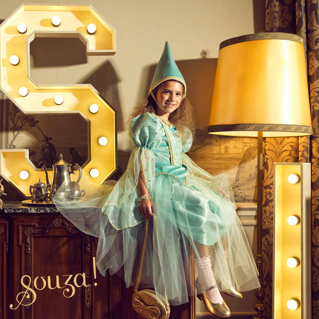 Girl wearing sky-blue velvet medieval princess hat with gold stars and veil, smiling in elegant dress-up setting