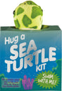 Plush mini sea turtle peeking out of a blue box labeled Hug a Sea Turtle Kit with an educational guide inside.