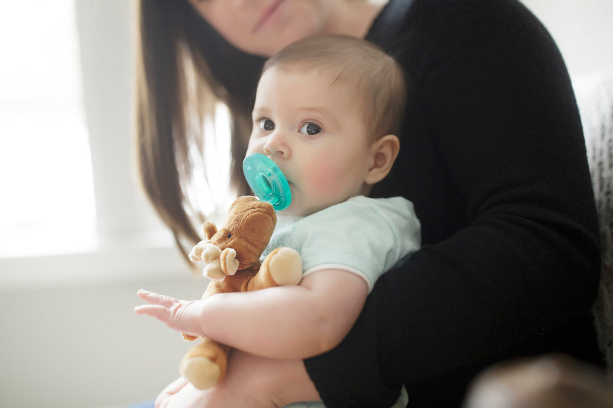 Baby holding a plush moose pacifier with WubbaNub | Moose in a caregiver's arms at home.