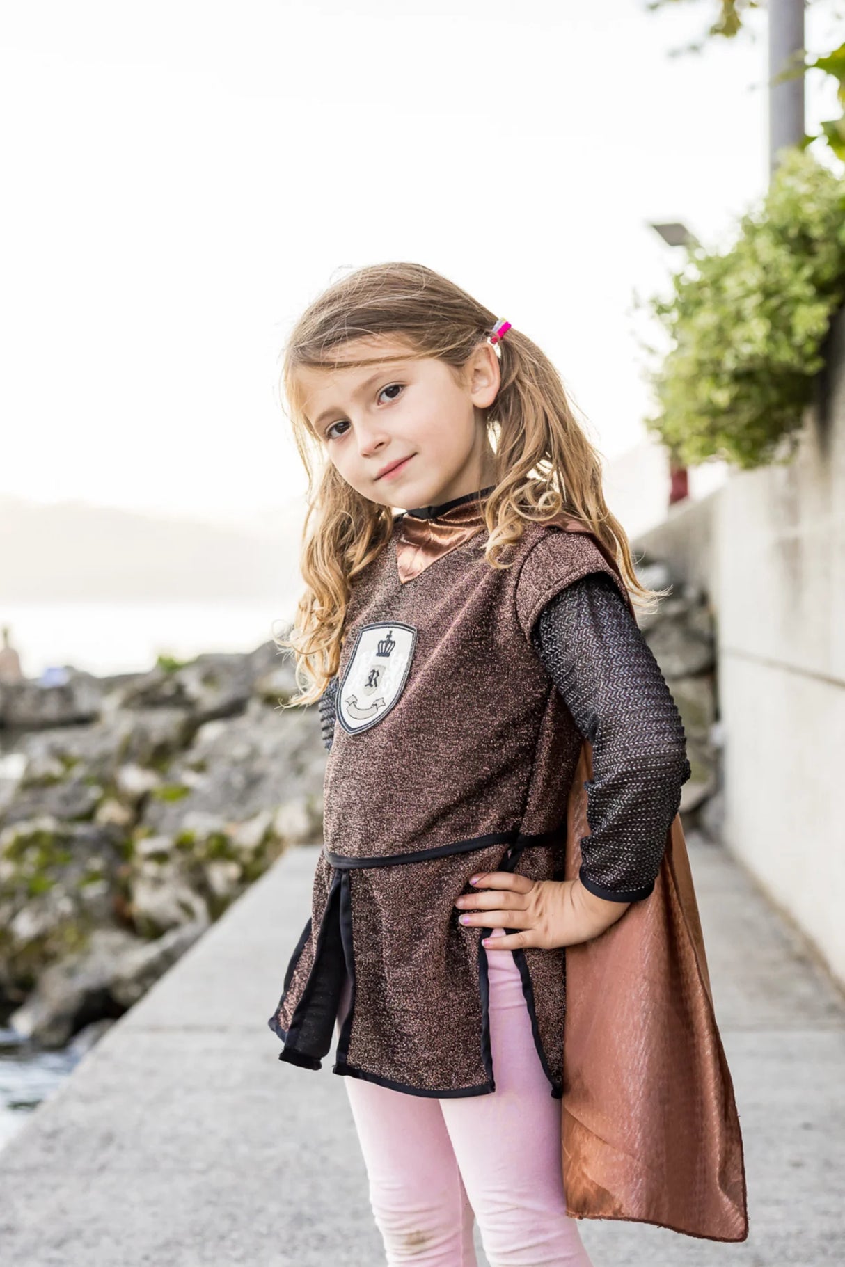 Child wearing Brilliant Copper Knight Tunic with Cape featuring lion emblem and chainmail sleeves by the water.