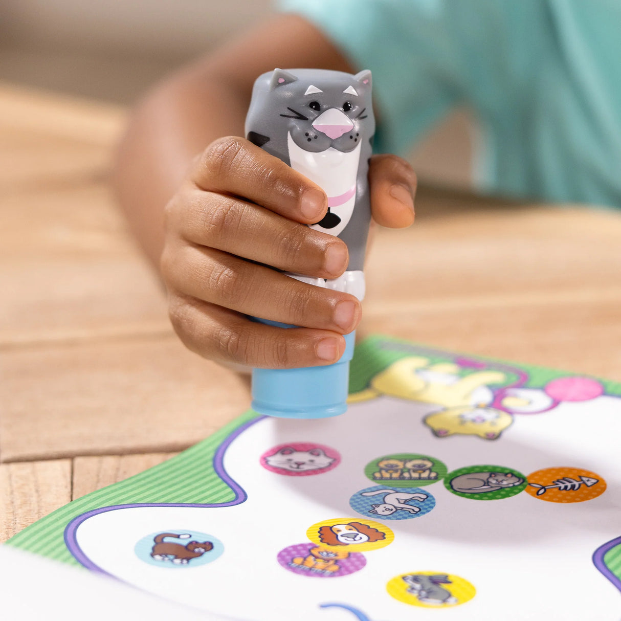 Child's hand using Sticker WOW! Cat stamper to create colorful pet-themed stickers on activity sheet.