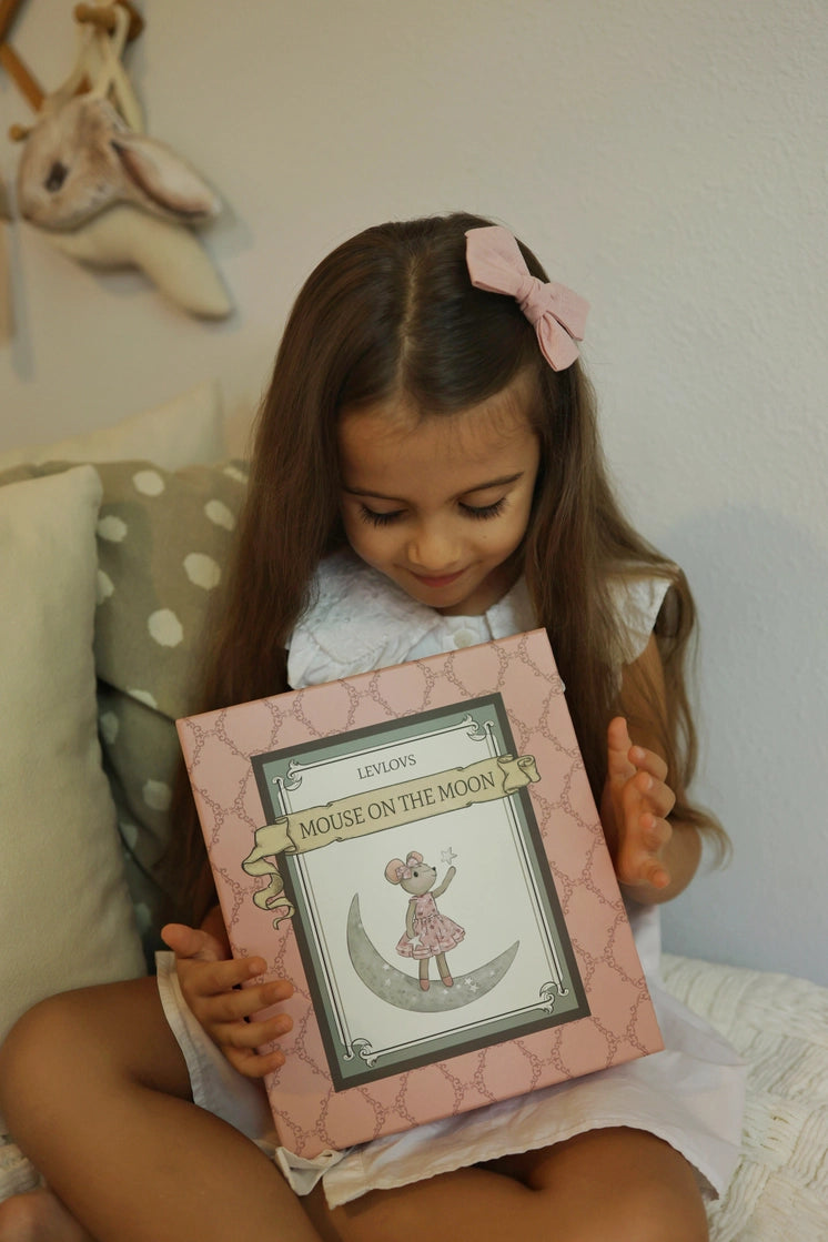 Little girl holding a Levlovs Sweet Dreams Mouse packaged box featuring a mouse standing on a moon illustration.