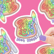 Hand holding a Spread Love Toast Sticker with rainbow colors on a pink background, durable vinyl material.