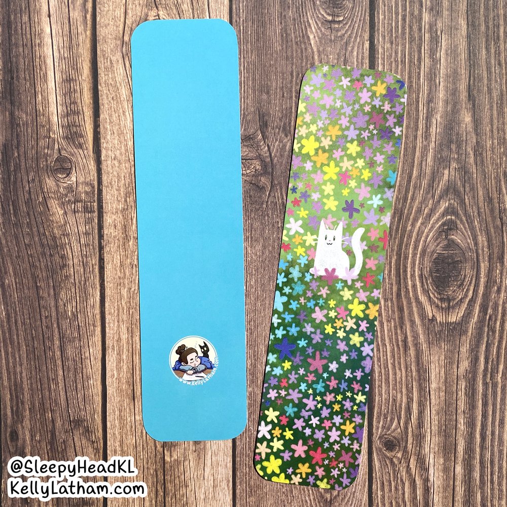 Cat & Flowers Bookmark showing a white cat among colorful flowers on one side and solid blue with artist logo on the back.
