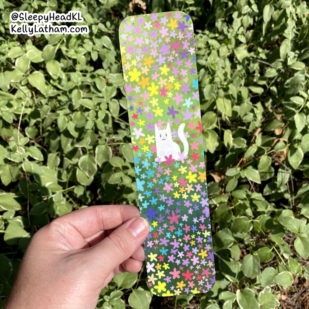 Hand holding Cat & Flowers Bookmark featuring a white cat amid colorful flowers on glossy coated paper.