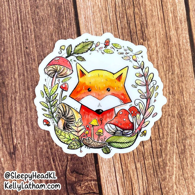Fox & Mushroom Wreath Sticker featuring a cute fox surrounded by colorful mushrooms and leaves on a wooden background.