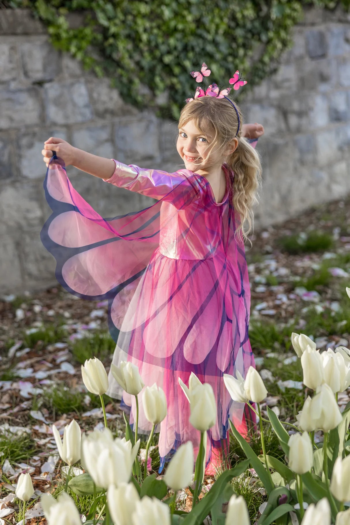 Little girl wearing Butterfly Twirl Dress & Wings | Pink with flowing butterfly wings and matching headband outdoors.
