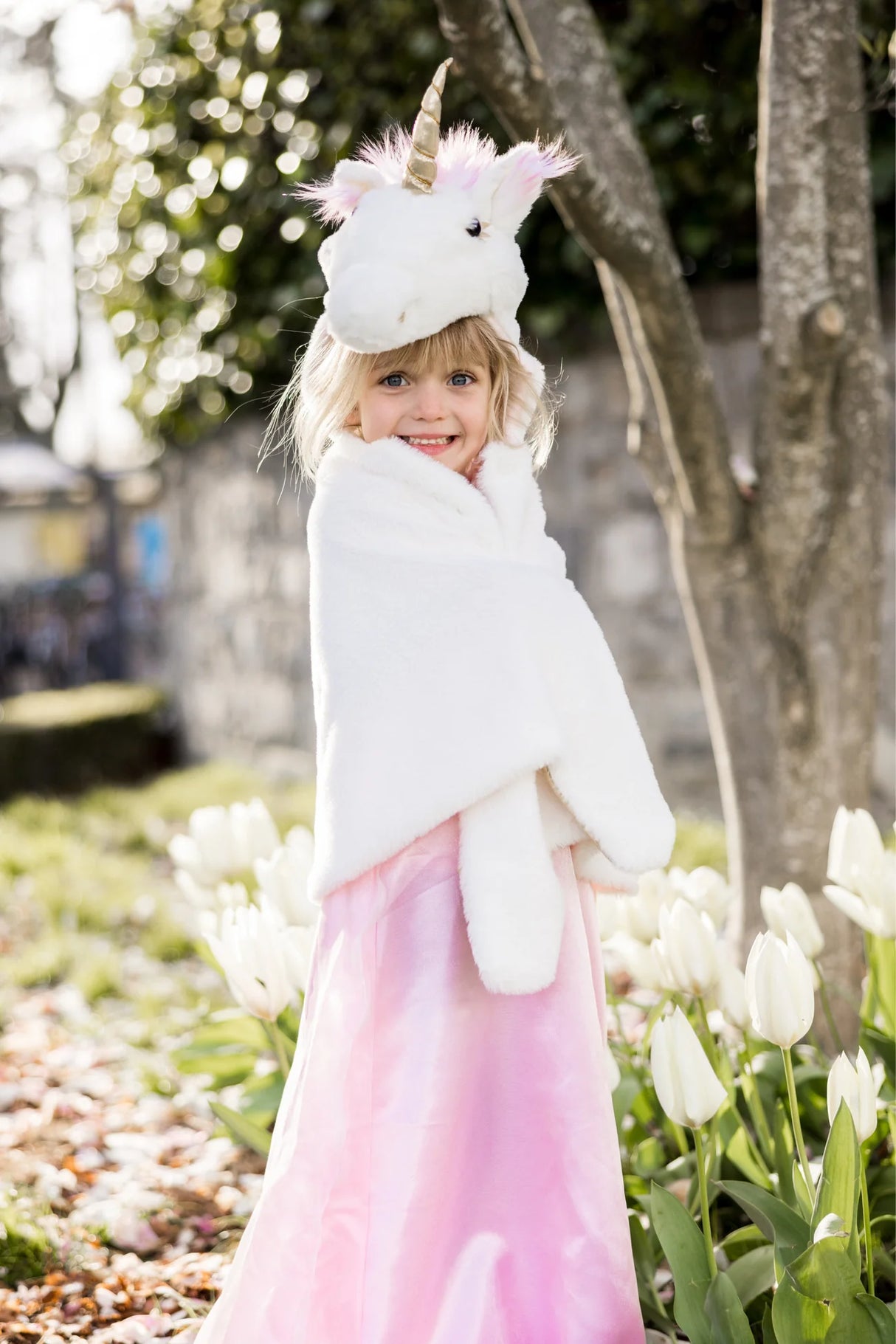 Child wearing the Unicorn Cuddle Cape | Size 4-6 in white faux fur with unicorn hood and pink dress outdoors.