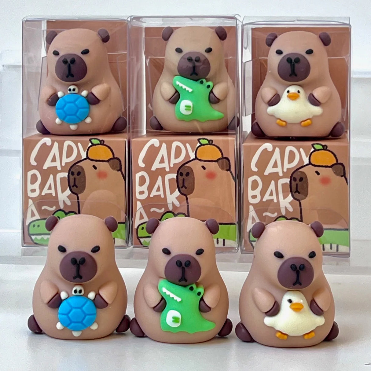 Set of cute capybara pencil sharpeners holding small blue turtle, green crocodile, and white duck toys in clear packaging.