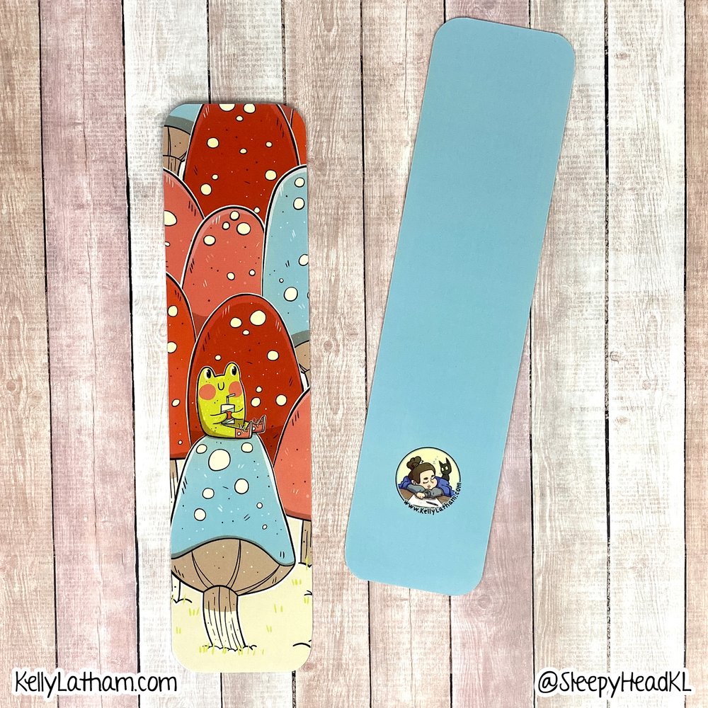 Frog & Mushrooms Bookmark showing a cute frog sipping juice atop colorful mushrooms with a solid blue back.