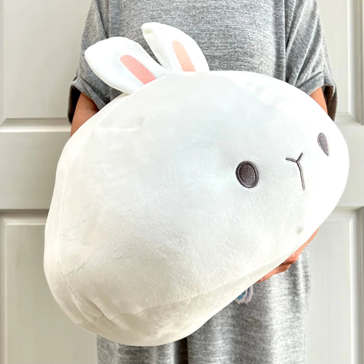 Person holding a soft, white Jumbo Round Rabbit plush with cute facial features and pink-lined ears.