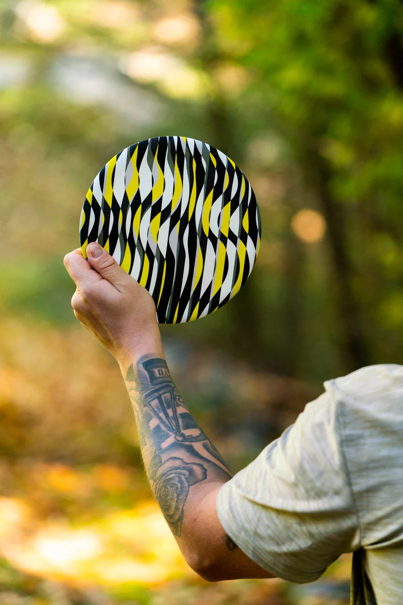 Person holding a black, white, and yellow patterned Waboba Wingman Disc PRO flying disc outdoors.