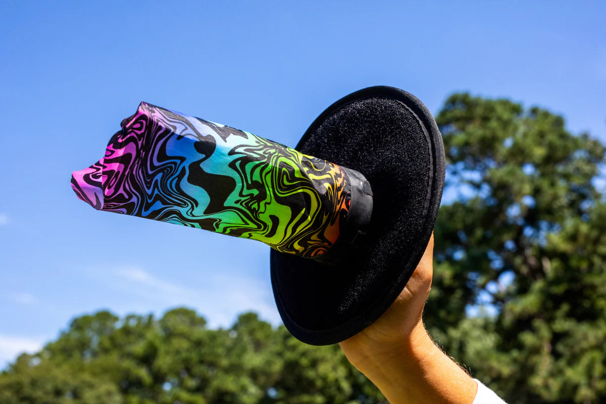 Hand holding colorful Waboba Throwback velcro AIRLYFT glider paddle against blue sky outdoors.