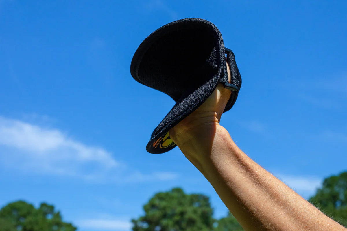 Hand holding a black velcro paddle in clear blue sky, Waboba Throwback paddle game accessory.
