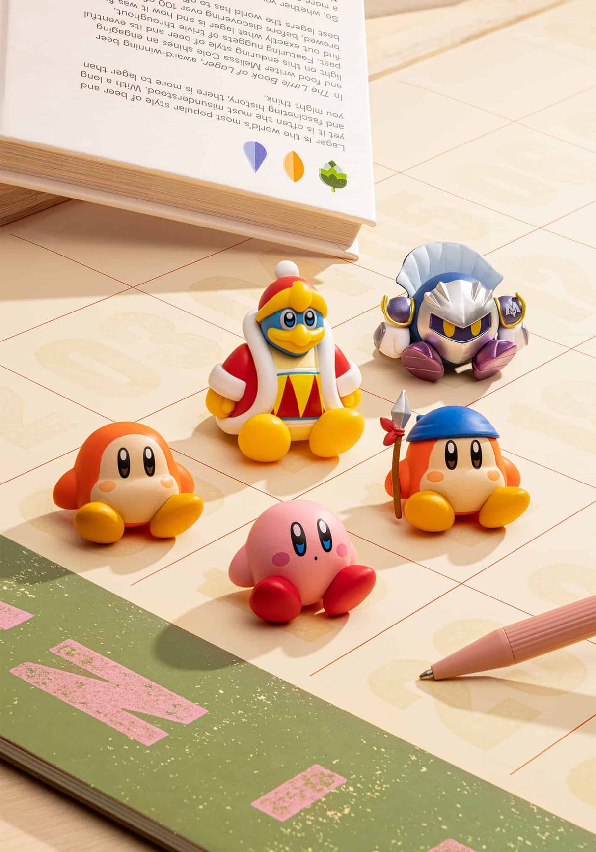 Kirby Sitting Blind Box featuring collectible sitting figures of Kirby and friends on a desk near a book and pen.