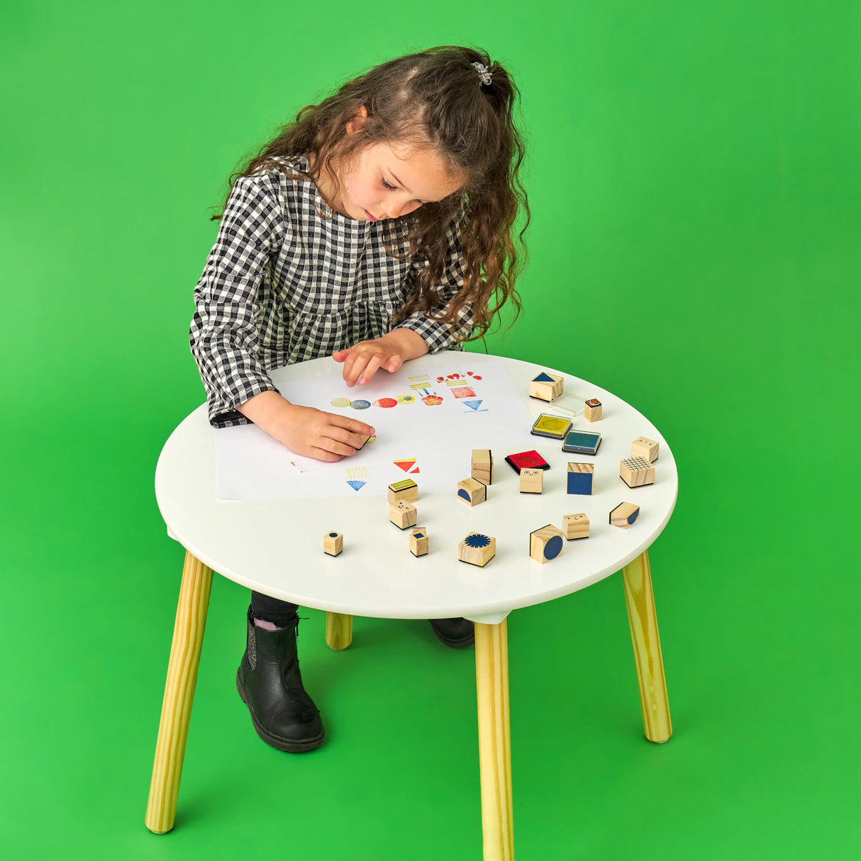 Young girl using the Make, Create & Play Stamp It! Set with stamps and ink pads on a white table.
