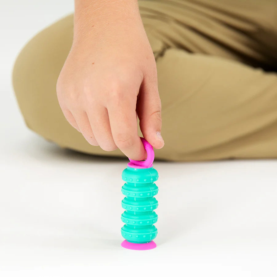 Child's hand playing with a turquoise and pink Krumples Fidget toy on a white surface.
