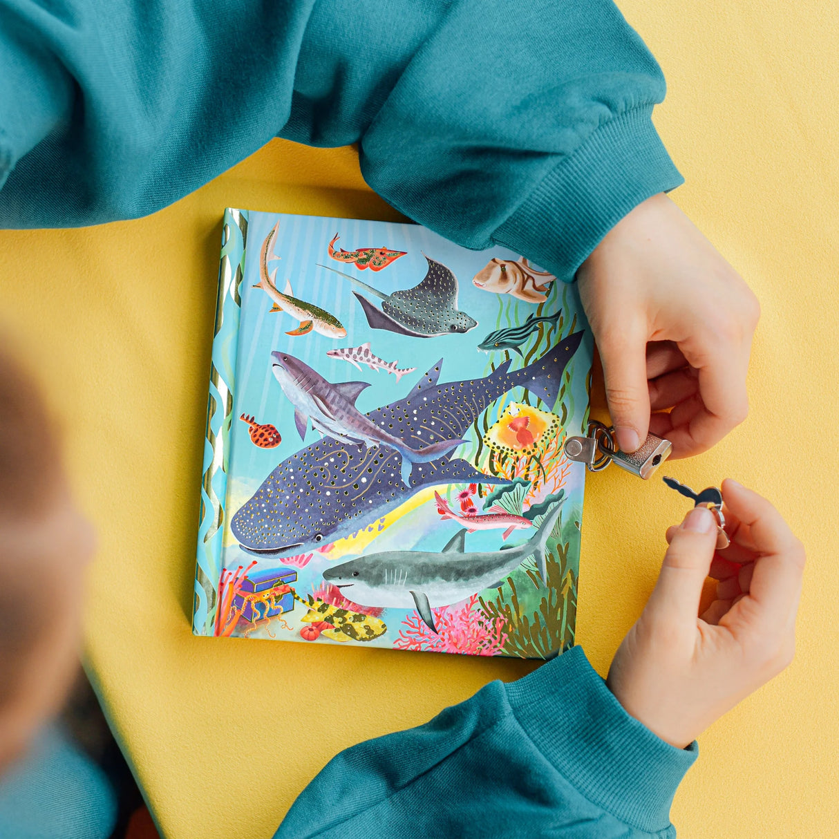 Hands holding keys unlocking the Sharks & Friends Diary with vibrant sea creature illustrations on cover.