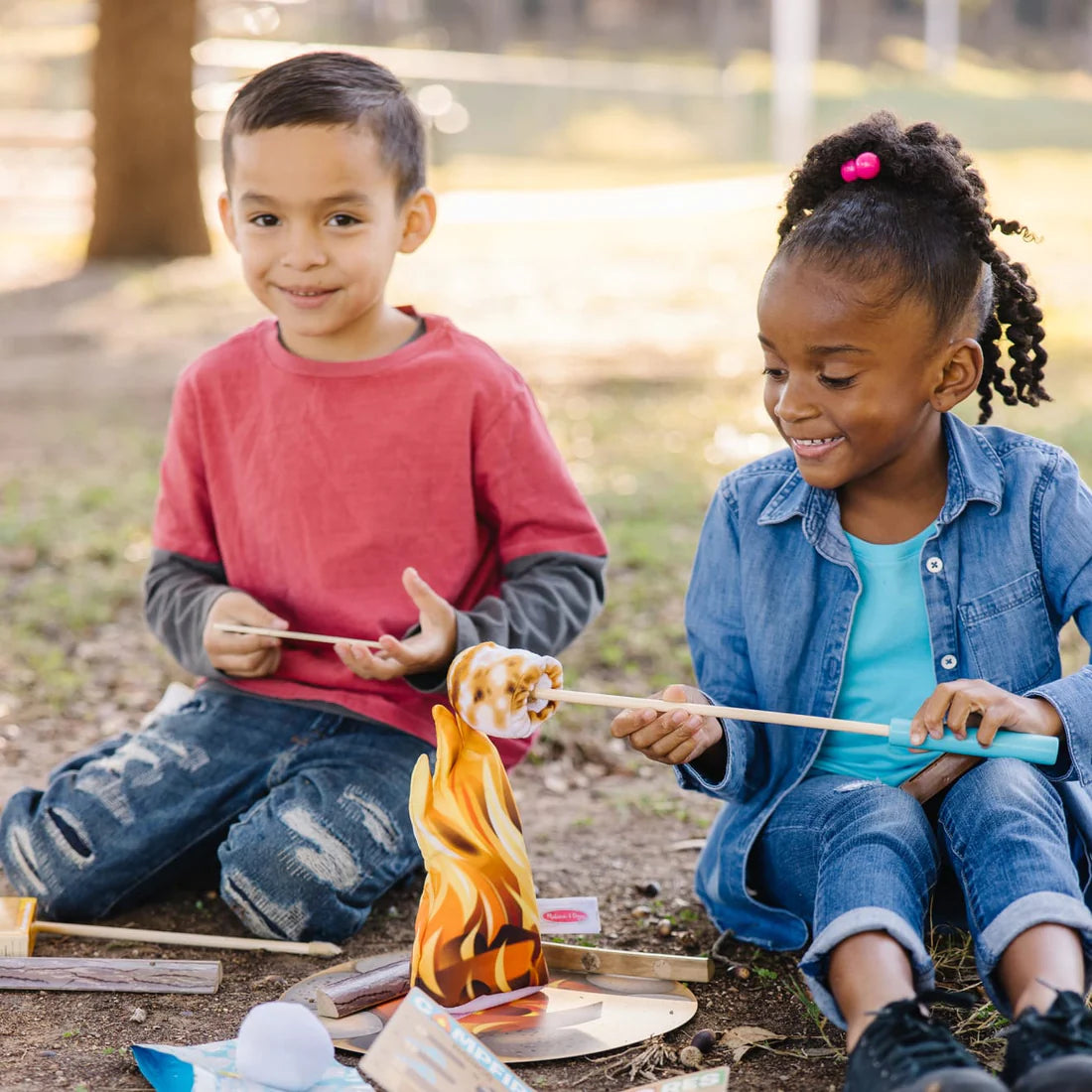 Two children playing outdoors with the Let’s Explore Campfire S'mores Play Set and toasting marshmallows.