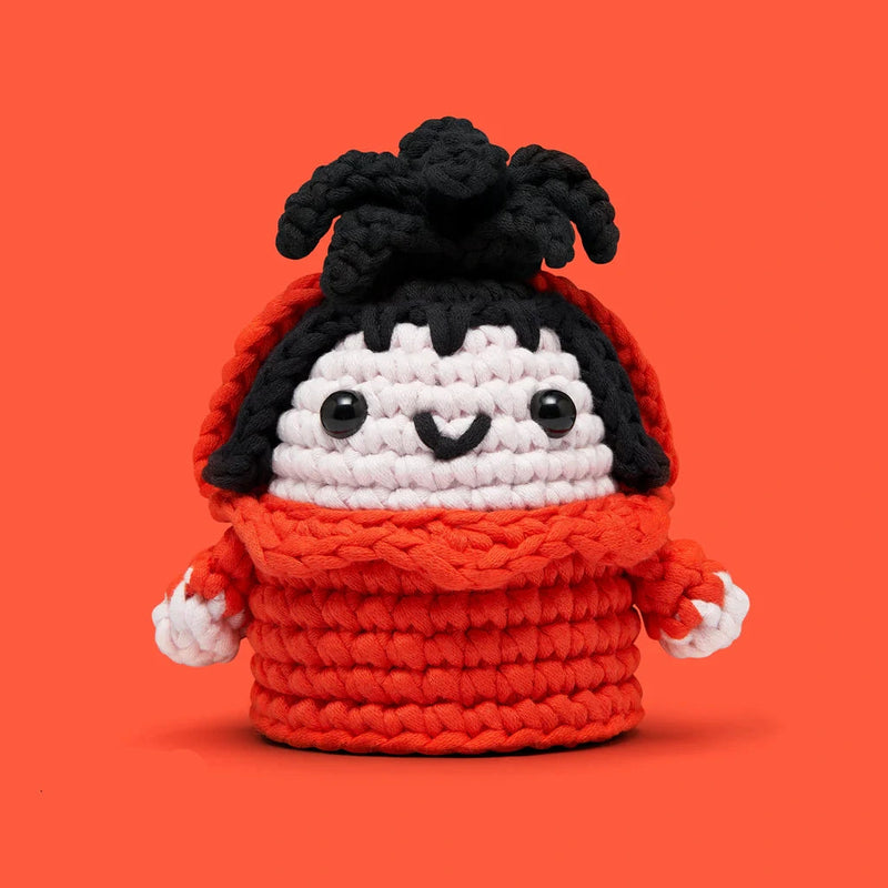 Handmade crochet doll with black hair and bright red outfit on an orange background smiling warmly