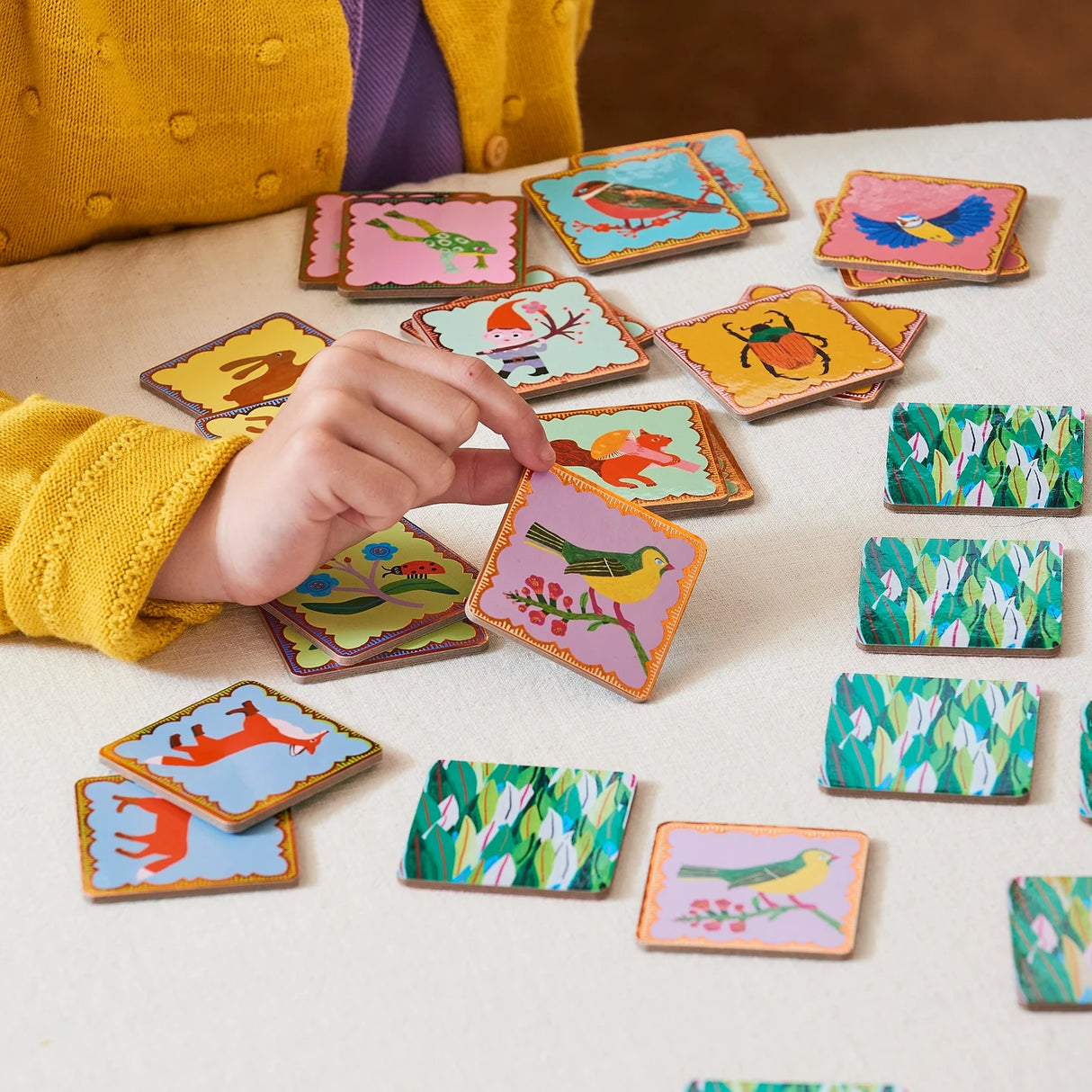 Child playing with Memory & Matching Woodland cards featuring animal illustrations and copper gilded edges on a table.