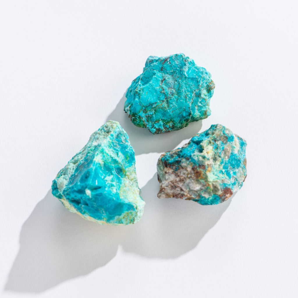 Three rough chrysocolla stones with vibrant blue-green hues on a white background, Rock | Rough Chrysocolla product.