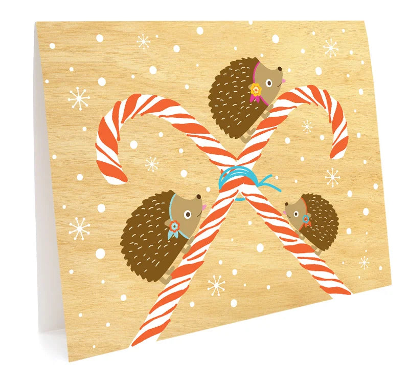 Peppermint Hedgehog Holiday Card with two candy canes and three hedgehogs on a snowy wood background.