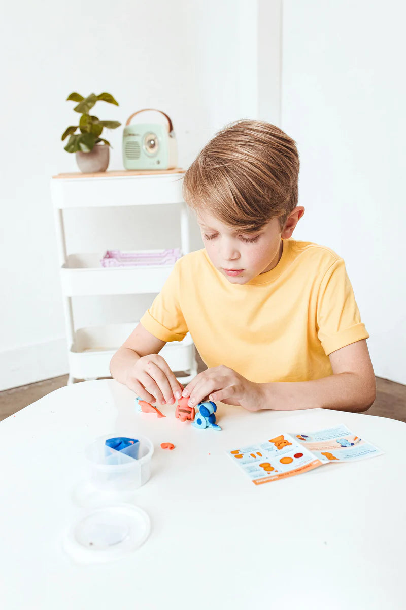 Child using Creatibles Air Dry Clay Kit | Pet BFFs to sculpt orange kitten and blue dog figures with instructions on table.