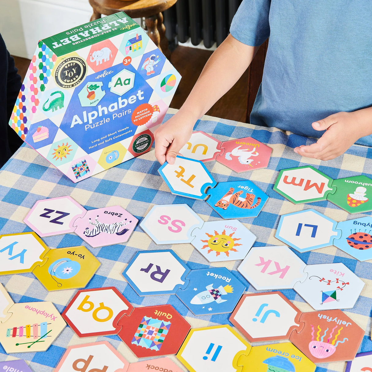 Child assembling colorful Alphabet Puzzle Pairs with hexagon pieces featuring letters and matching illustrations.