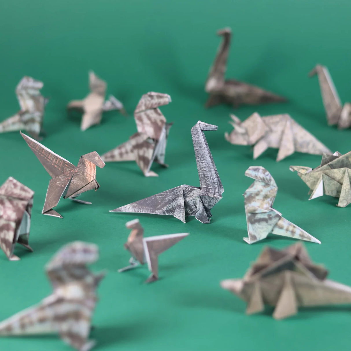 Folded origami dinosaurs crafted from patterned paper displayed on a green surface, showcasing various prehistoric creatures.