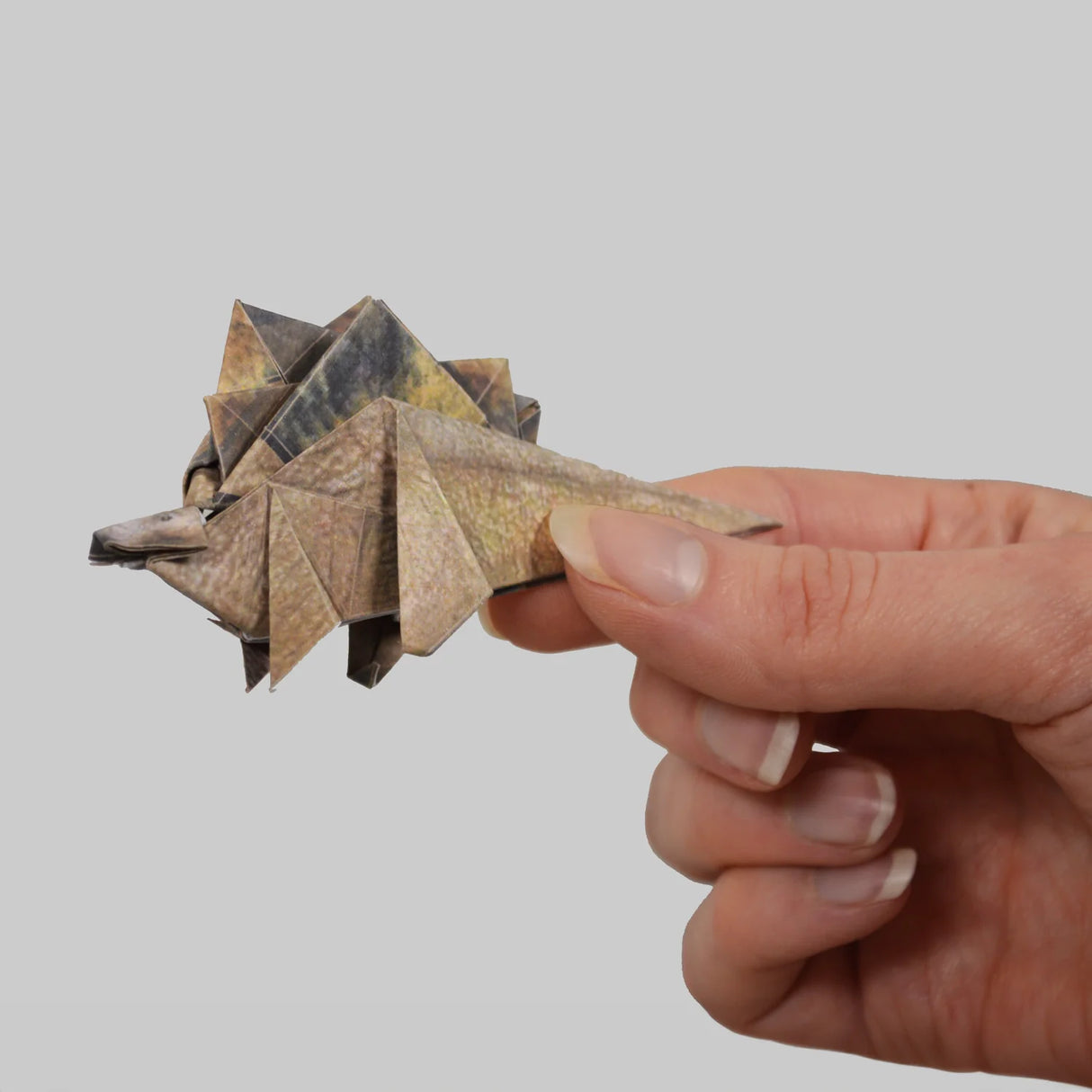 Hand holding a folded origami dinosaur model with realistic textures on grey background