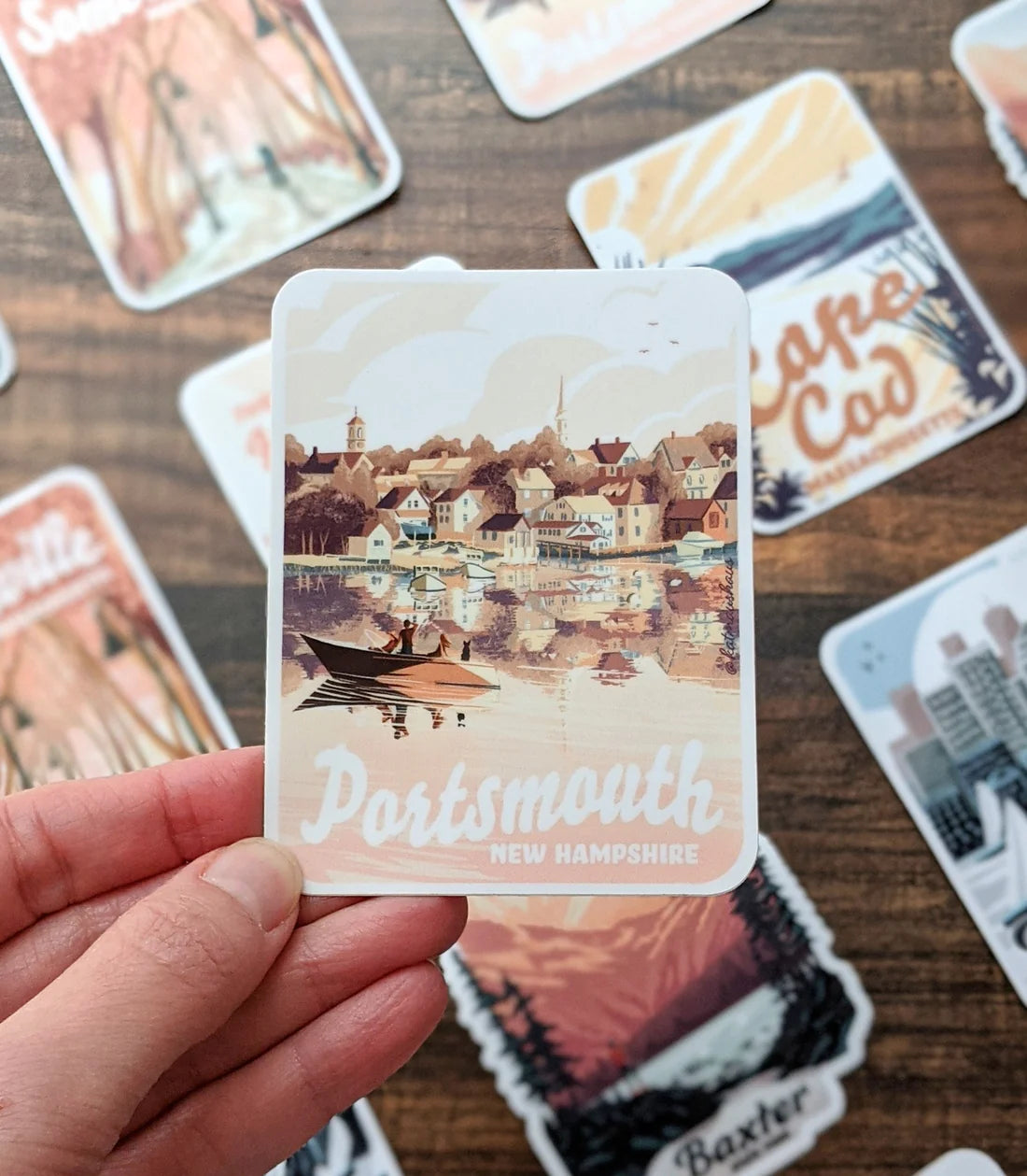 Hand holding Portsmouth NH Houses Sticker showing a charming waterfront town scene in muted colors.