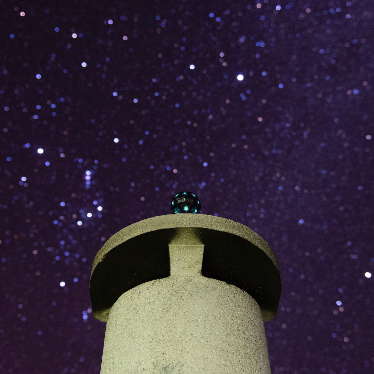 Moon Ball | Dark Side of the Moon with metallic dots resting on a stone pillar under a starry night sky.