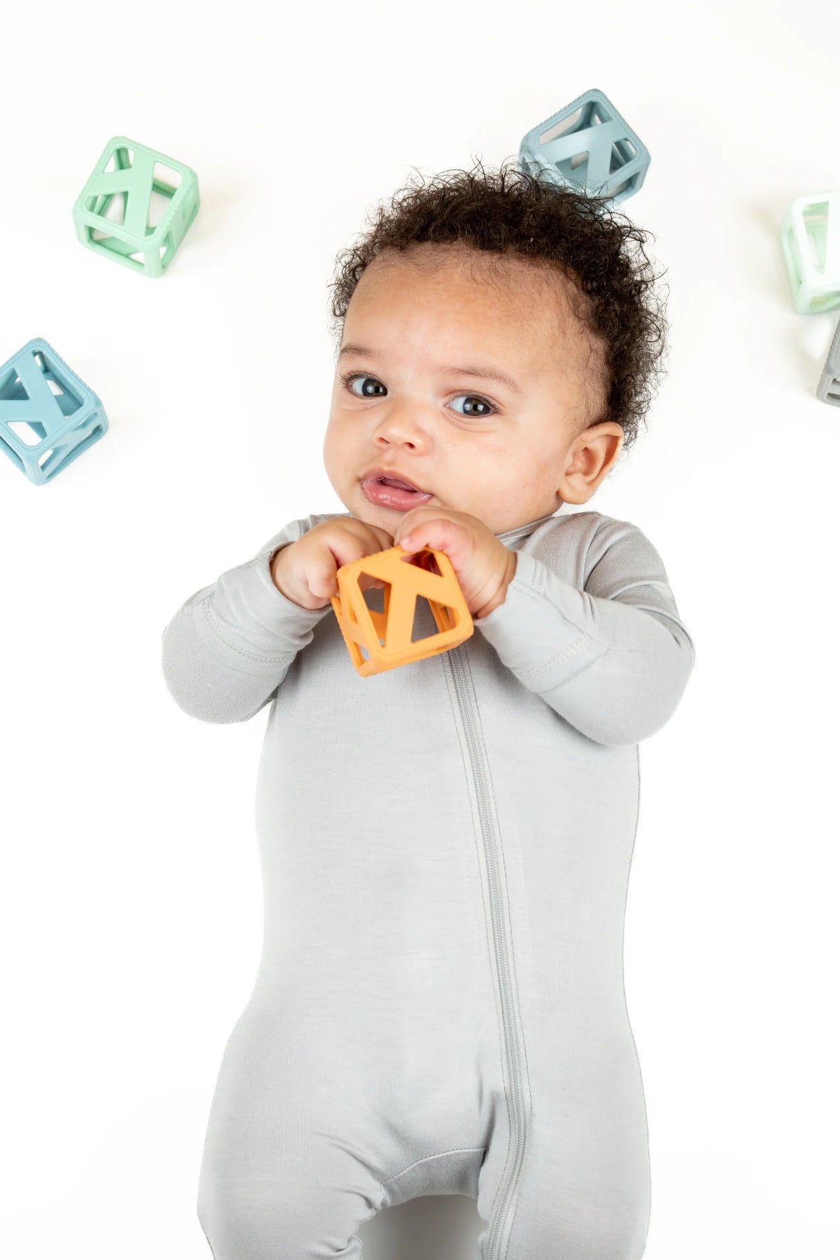 Baby holding an orange Stack & Chew Earthy Cubes teething toy surrounded by colorful stackable silicone cubes.
