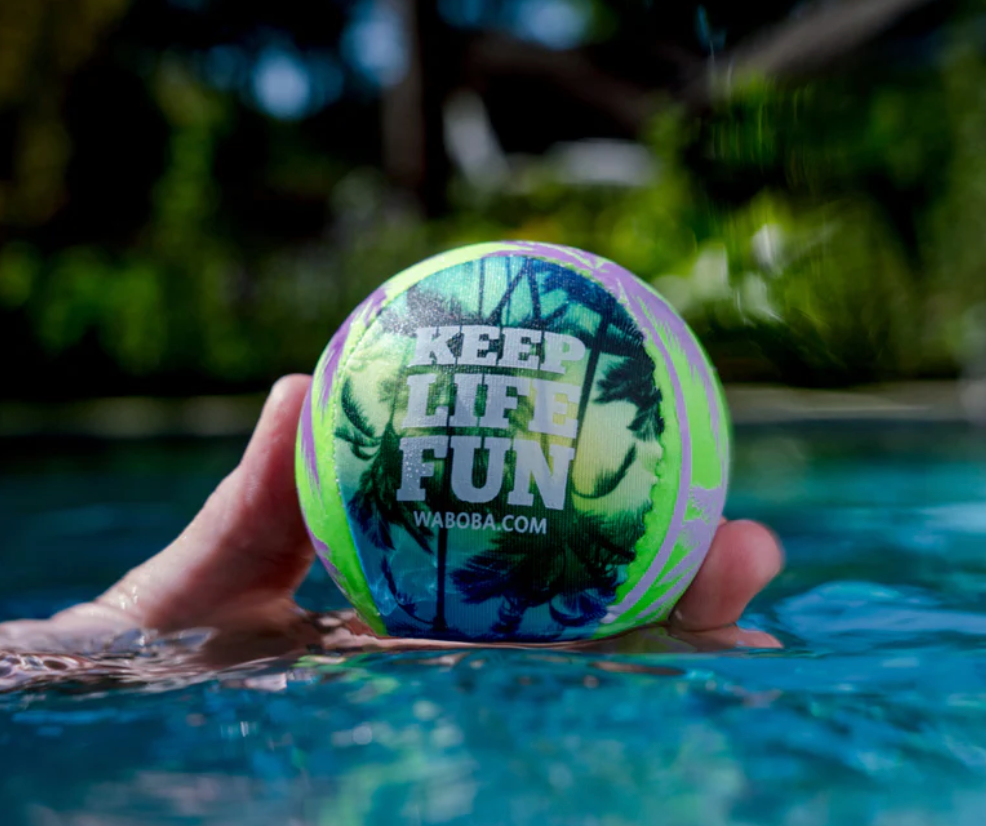 Hand holding a colorful Waboba SOL Ball floating on water with a tropical design and "Keep Life Fun" text visible.
