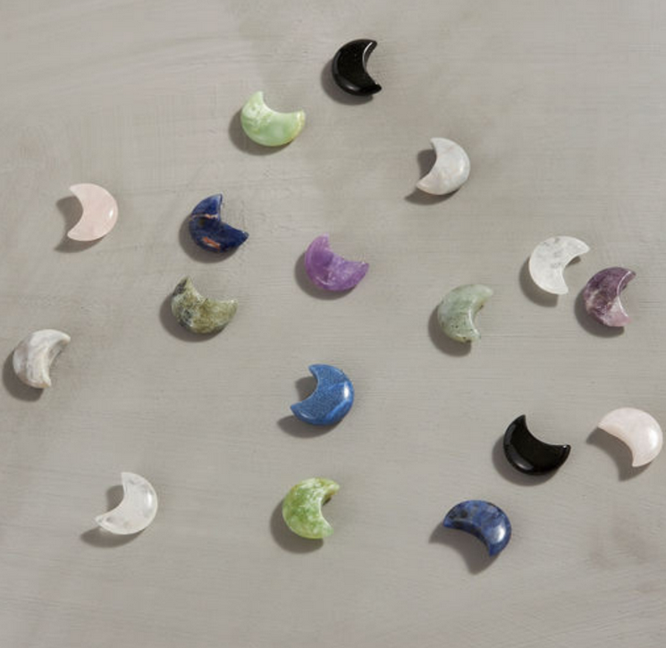 Carved Moon crystals in assorted types and colors, scattered on a light surface, showcasing their unique shimmer.